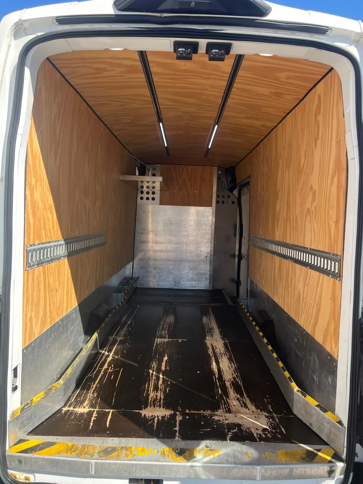 Inside a Ford Transit cargo area with plywood-lined walls, floor and roof rails